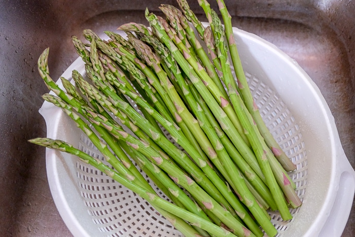 green asparagus spears in white strainer in sink getting washed