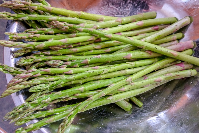 raw asparagus in silver bowl coated in oil and spices