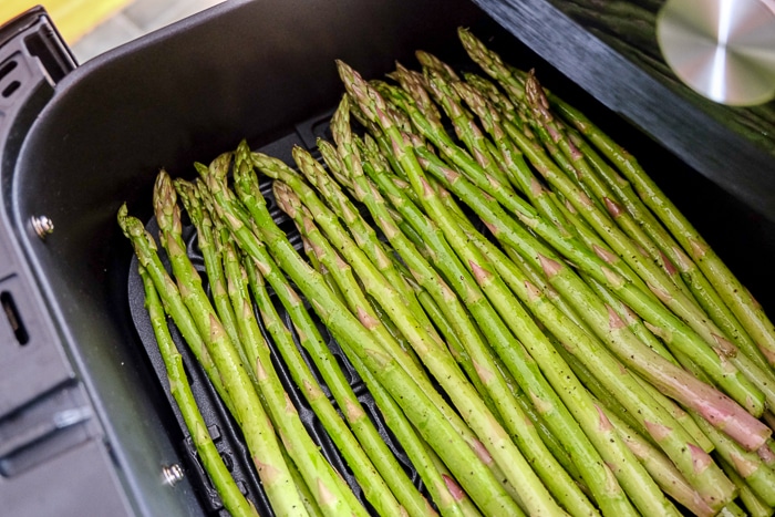 raw green asparagus in black air fryer tray