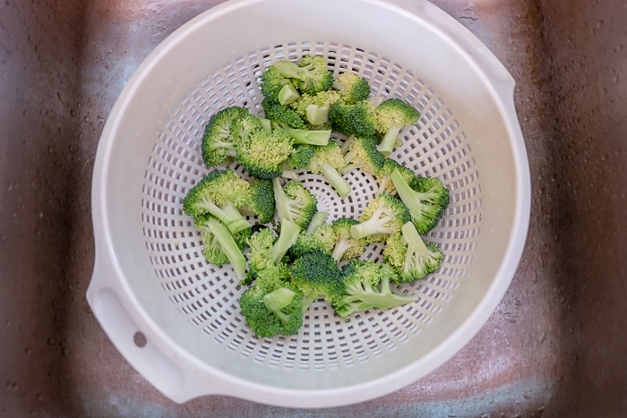 raw broccoli in white strainer in sink
