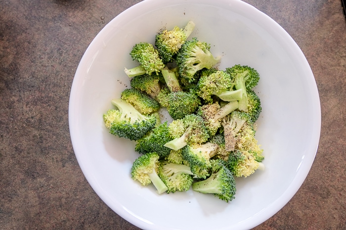 raw broccoli in white bowl with oil and spices