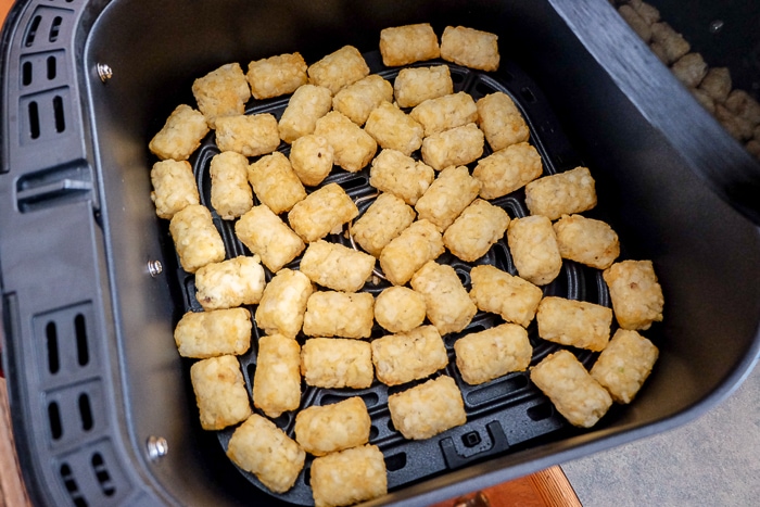 tater tots spread out on black air fryer tray