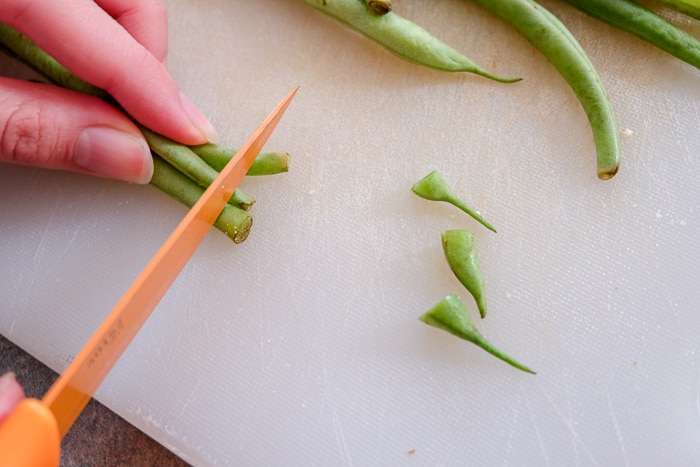 trimming ends off green beans with orange knife on cutting board