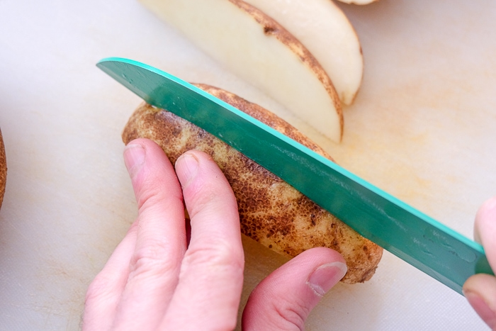 cutting potato wedge with green knife on white board