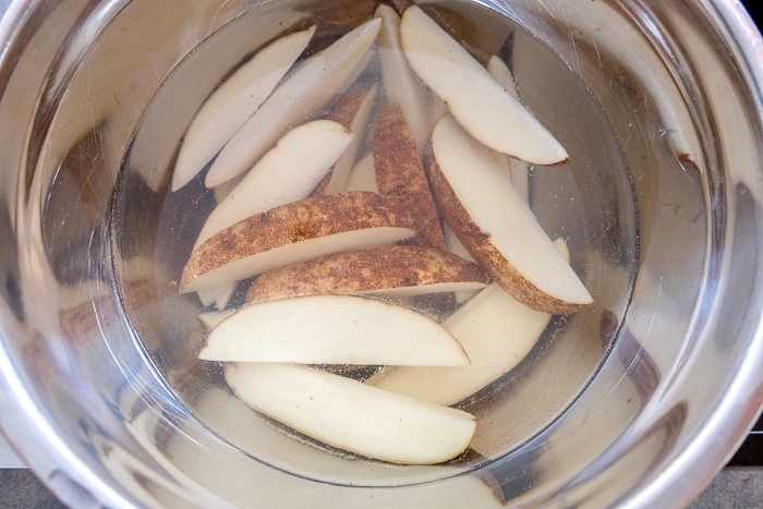 raw potato wedges sitting in clear bowl of hot water