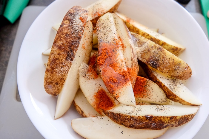 dry spices on raw potato wedges in white bowl