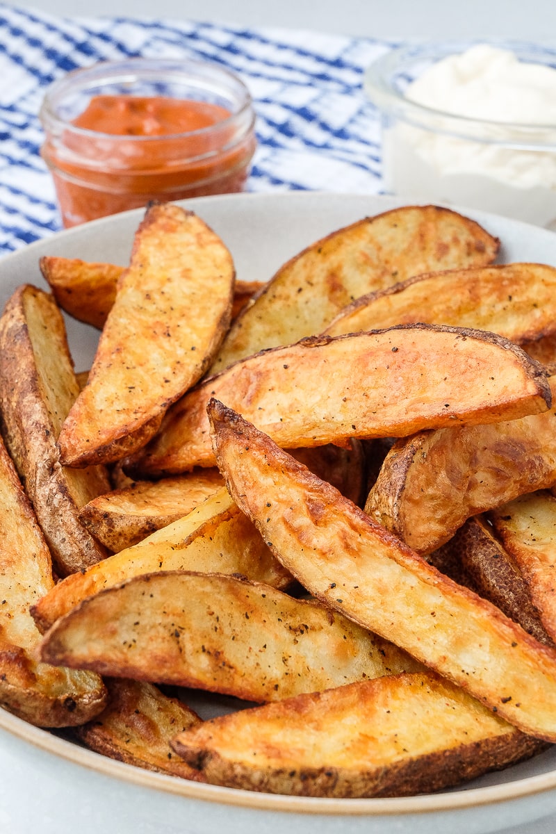 crispy potato wedges in bowl with dipping sauces behind