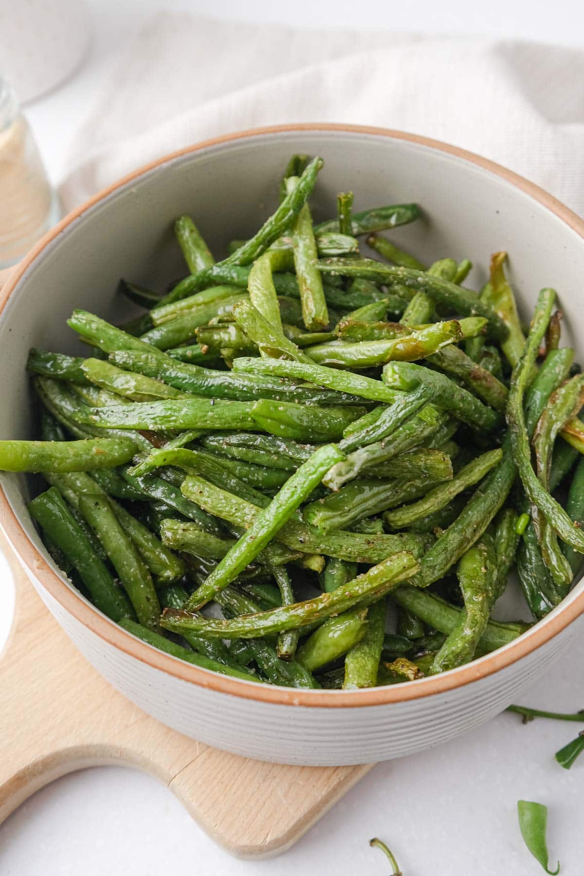 cooked green beans in serving dish on wooden board with cloth behind.