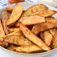 crispy potato wedges in bowl with dips behind
