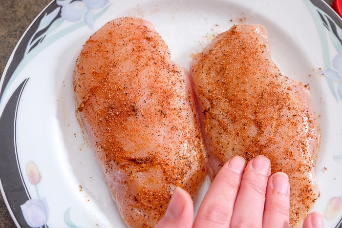 rubbing dry spices on chicken breast on plate