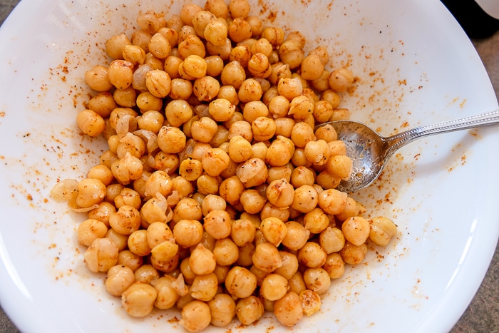 chickpeas coated in oil and spices in white bowl with spoon.