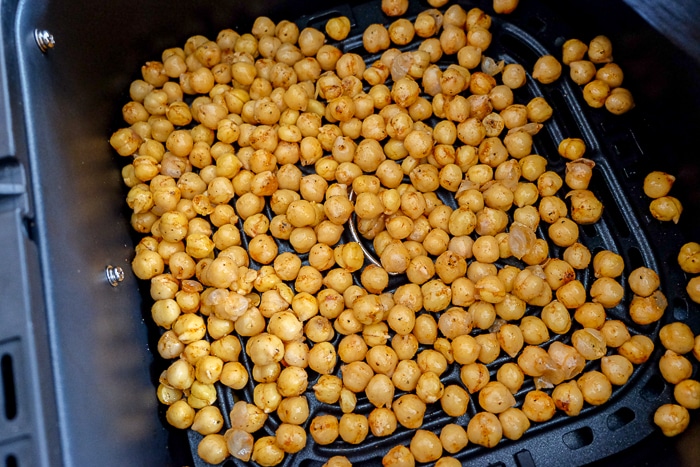 seasoned chickpeas spread out in black air fryer basket.