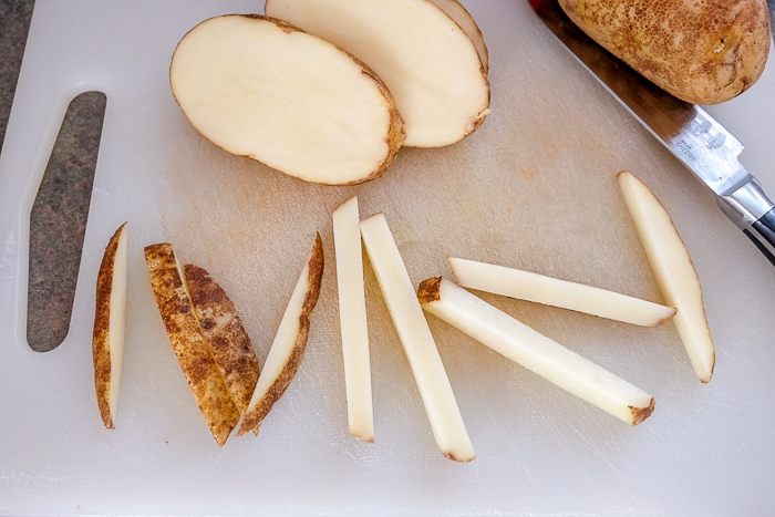 raw potatoes cut into french fries on white cutting board