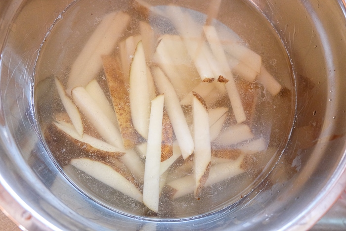 fresh cut french fries soaking in water in metallic bowl