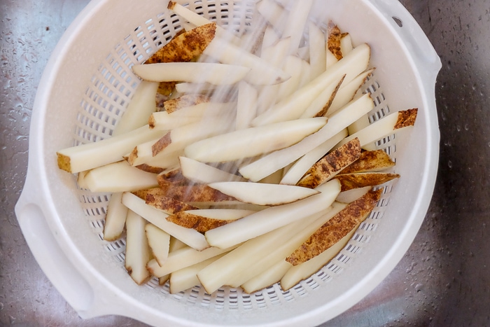 rinsing fresh cut fries with water in white strainer