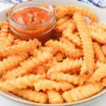 golden crinkle cut fries on plate with dipping sauce
