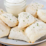 bowl of crispy pierogies with cup of sour cream on wooden board