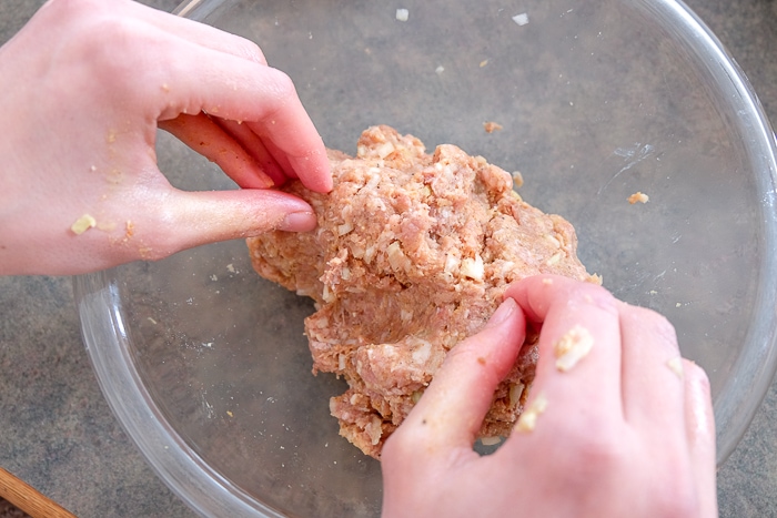 raw meat in glass bowl with hands mixing.