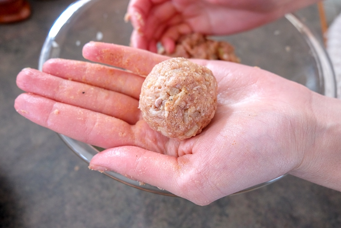 rolled meatball in hand above clear glass bowl.
