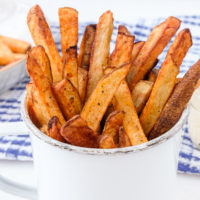 crispy french fries in cup with dipping sauce behind