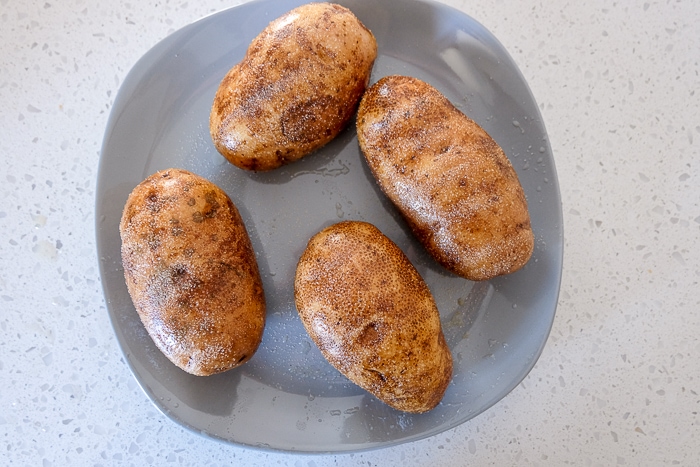four raw russet potatoes on blue plate on white counter top