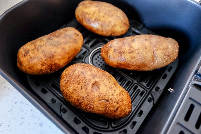 four whole raw potatoes in dark air fryer tray