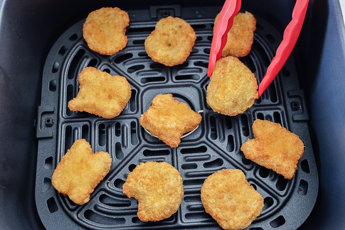 turning chicken nuggets with red tongs in air fryer tray
