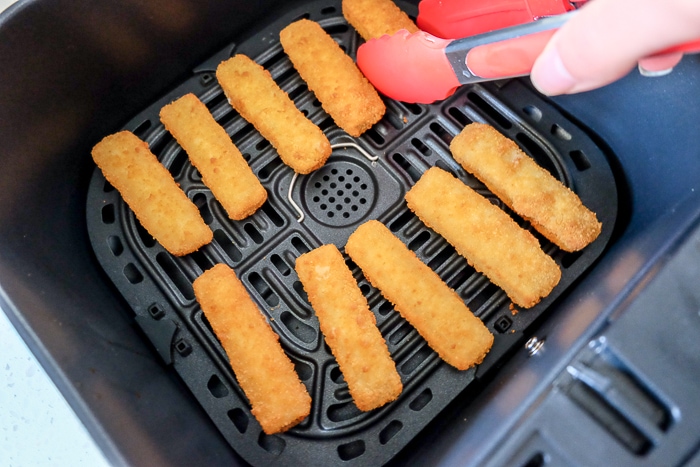 flipping frozen fish sticks in air fryer with red tipped tongs