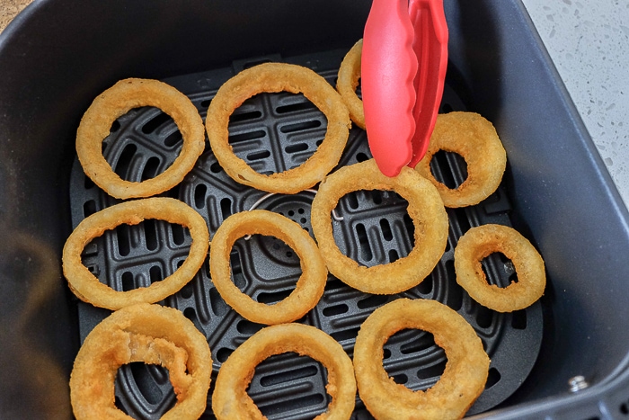 onion rings in air fryer flipped with red tongs