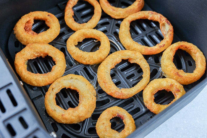 cooked crispy onion rings in black air fryer tray