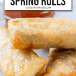 cooked spring rolls stacked in bowl with red dipping sauce in background and text overlay saying "air fryer frozen spring rolls"