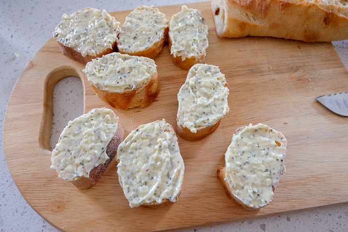 garlic butter spread thick on slices of bread on wooden cutting board