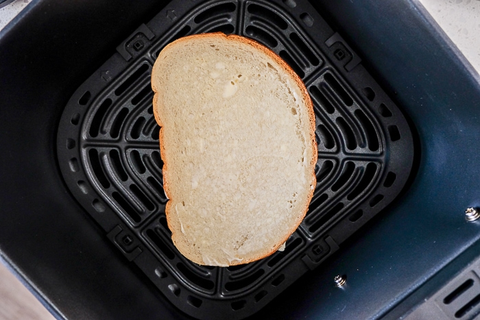 uncooked grilled cheese with mayo on bread in black air fryer tray
