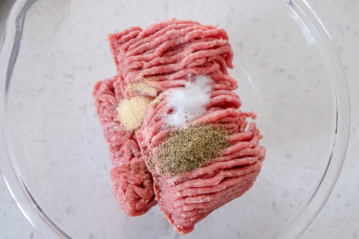 raw ground beef with spices in clear bowl