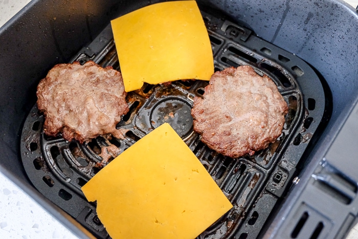 slices of orange cheese on cooked burgers in air fryer