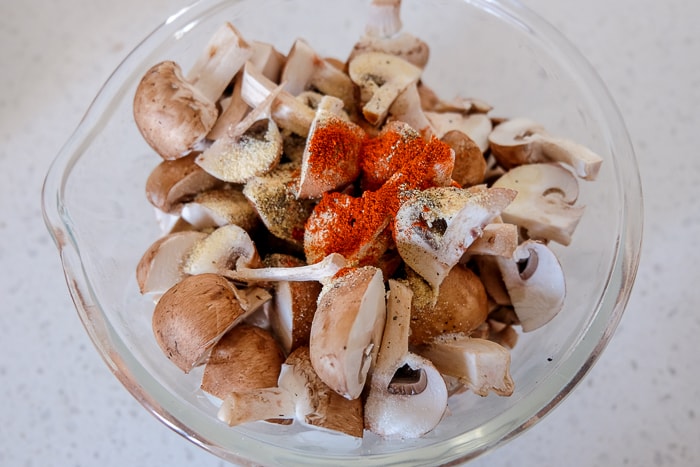 raw mushrooms cut up in clear glass bowl with spices on top