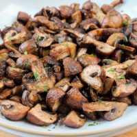 fried mushrooms with parsley in bowl on wooden board