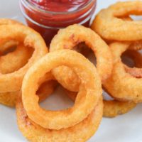 crispy cooked onion rings in bowl with dipping sauce behind