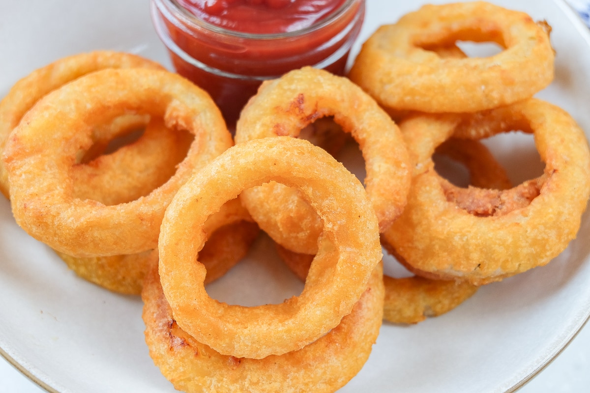 crispy cooked onion rings in bowl with dipping sauce behind