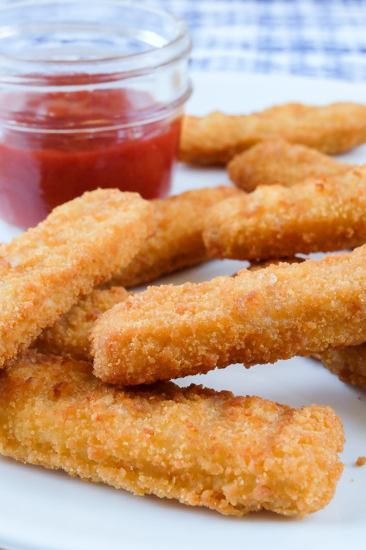 crispy fish sticks on white plate with ketchup behind