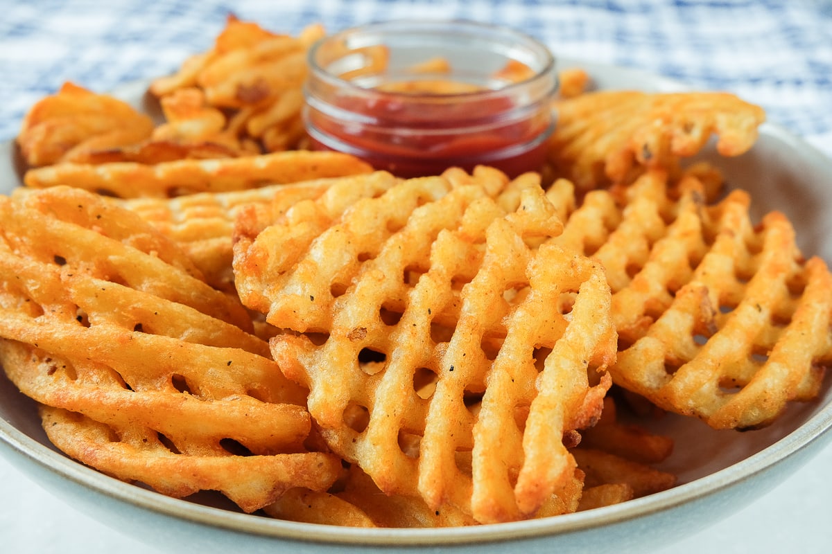 crispy waffle fries in bowl with ketchup behind