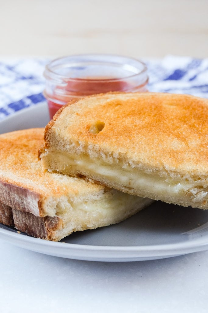 grilled cheese cut in half on plate with dipping sauce behind
