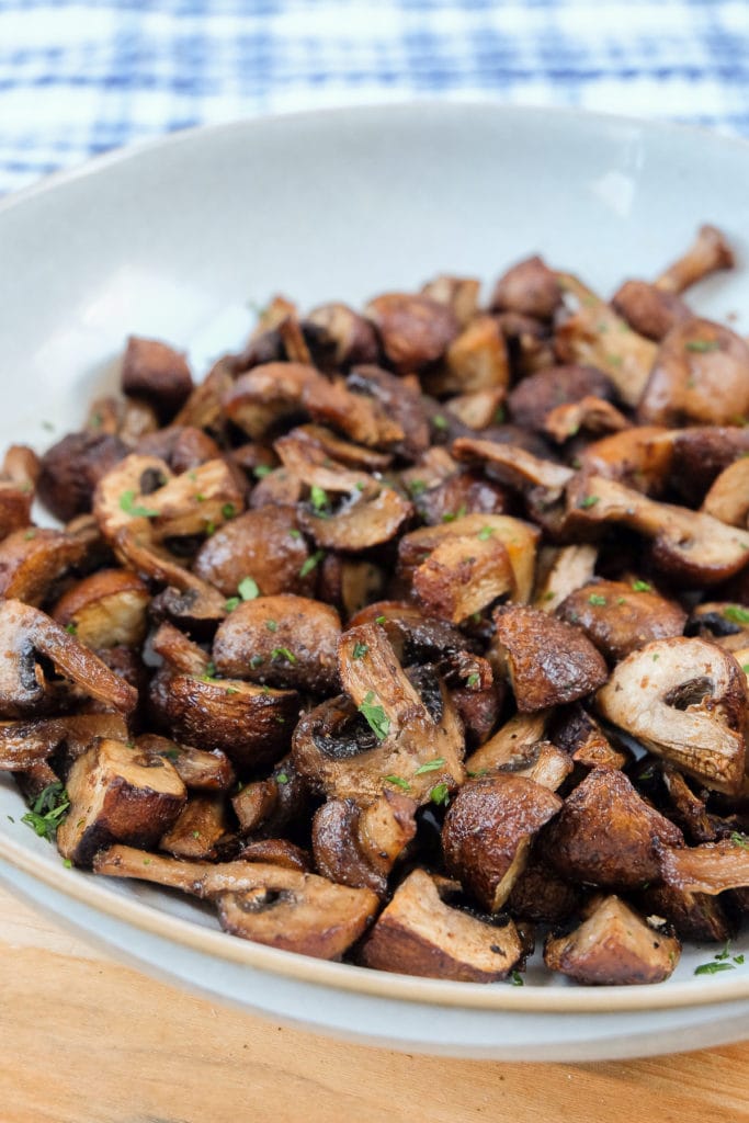 cooked mushrooms in bowl on wooden board with chopped parsley