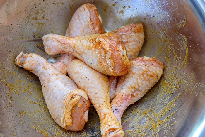 raw chicken drumsticks in metal bowl covered in spices and oil