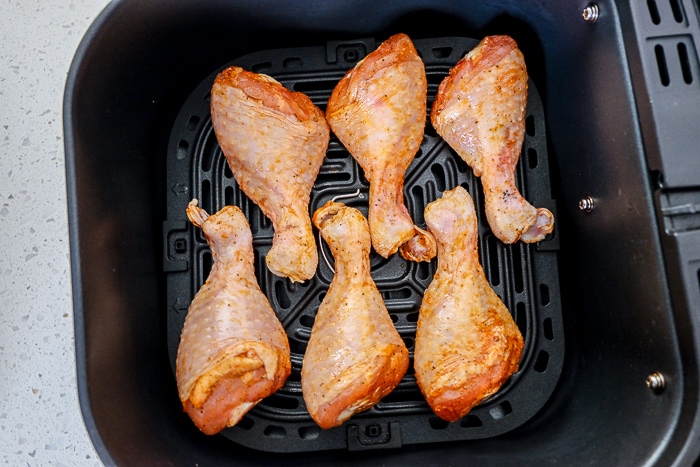 chicken drumsticks in black air fryer tray on white counter