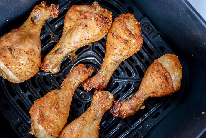 cooked chicken drumsticks in black air fryer tray