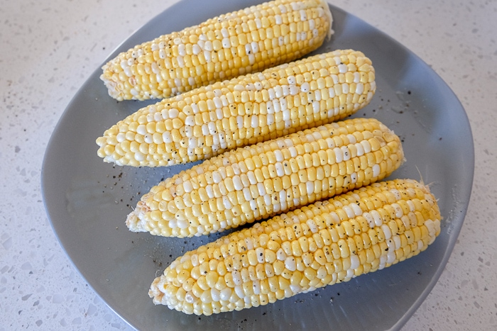 raw corn on the cob on grey plate on white counter
