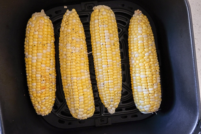 raw corn on the cob in black air fryer tray