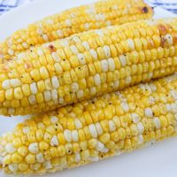 cooked corn on the cob on white plate on wood board
