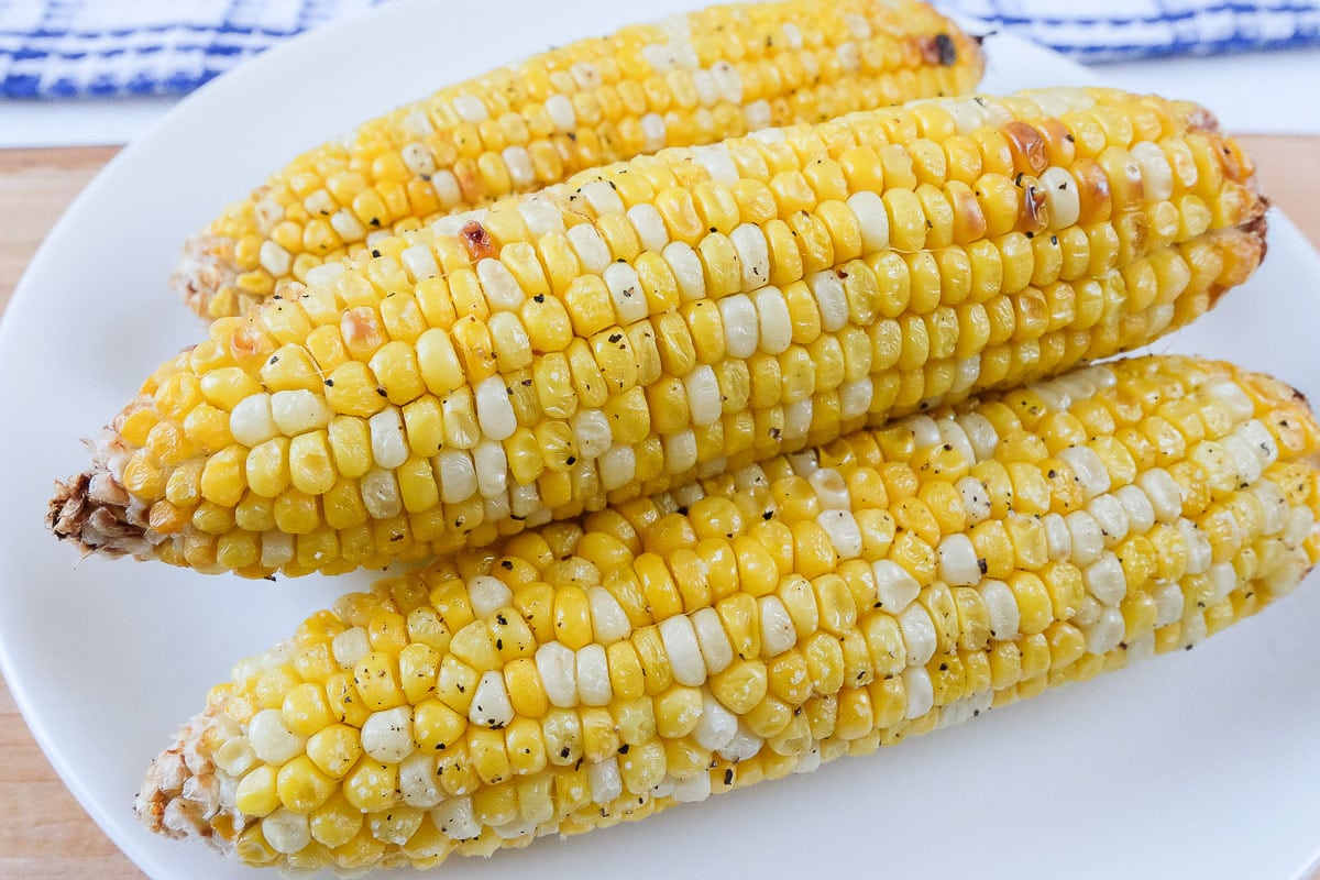 cooked corn on the cob on white plate on wood board